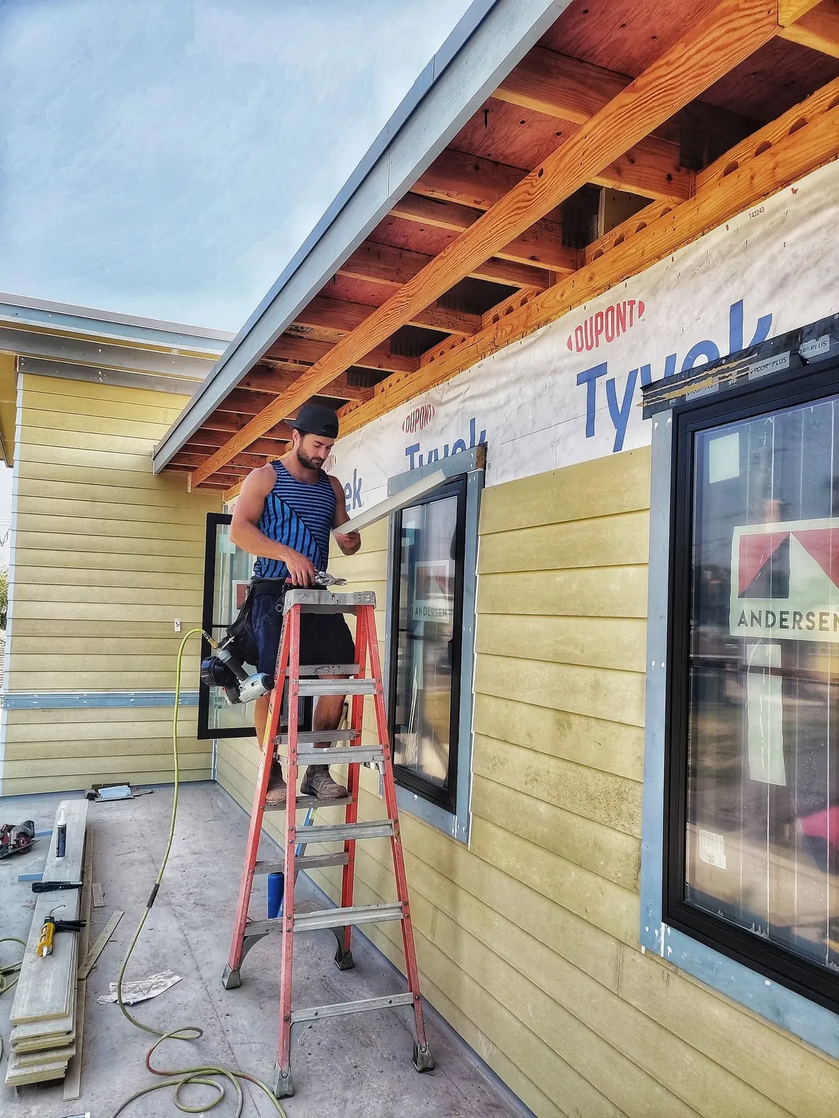 Worker installing exterior lap siding and window trim on a residential construction project
